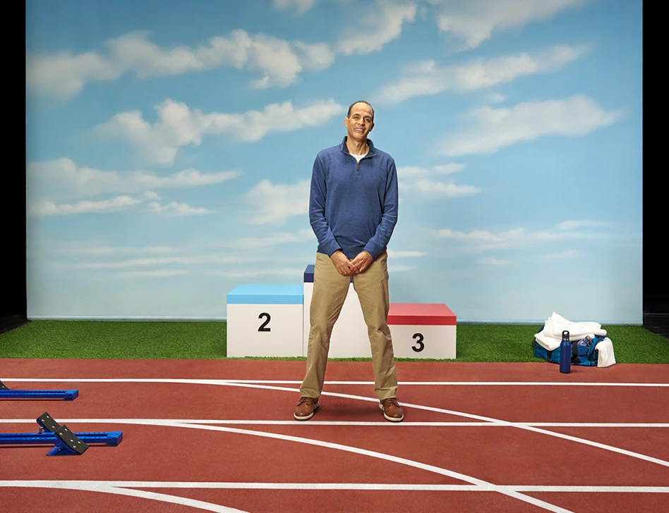Ray standing and smiling in front of a winner’s podium on a running track setting, sharing about his vitiligo repigmentation with Opzelura.