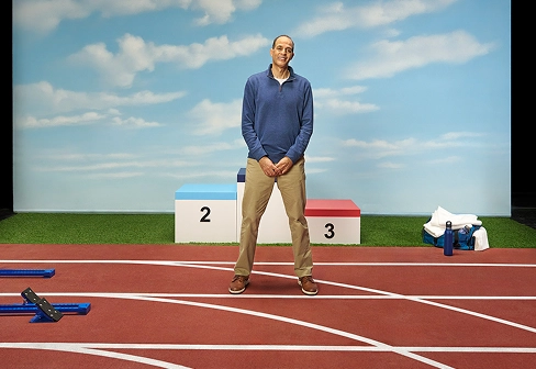 Ray standing and smiling in front of a winner’s podium on a running track setting, sharing about his vitiligo repigmentation with Opzelura.