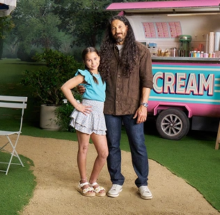 Piper and Adam standing in a park setting in front of an ice cream cart, discussing managing eczema at a young age with Opzelura.