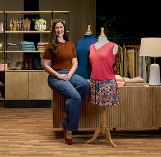 Sarah sitting and smiling in a department store setting, discussing her vitiligo repigmentation with Opzelura. 
