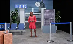 Carolyn smiling and standing in an airport setting, sharing her story about managing vitiligo with Opzelura.